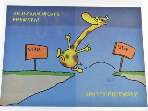 Eine Geburtstagskarte mit einer Giraffe, die an einer Klippe springt, umgeben von Verkehrsschildern mit den Aufschriften Weiter und Stop sowie dem Text Happy Birthday. Hersteller: Juwelier Harnisch.