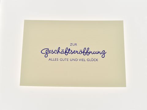 Eine dezent gestaltete Glückwunschkarte zur Geschäftseröffnung mit blauer Schrift, auf der steht: zur Geschäftseröffnung, alles Gute und viel Glück, Hersteller Juwelier Harnisch.