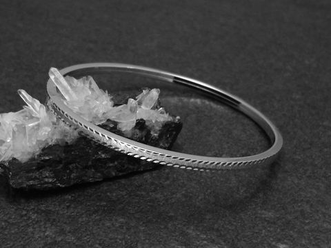 Silber Armreifen aufregend 3 mm rhodiniert 18 cm vom Hersteller Juwelier Harnisch auf schwarzem Untergrund neben kristallähnlichen Steinen platziert. Elegantes Design für modebewusste Trägerinnen.