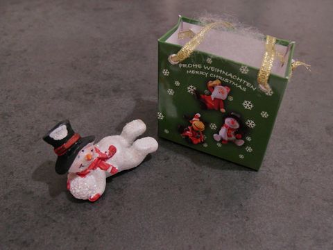 Schneemann mit Geschenktasche liegend neben einer Schneekugel, Hersteller Juwelier Harnisch, festliche Weihnachtsdekoration.