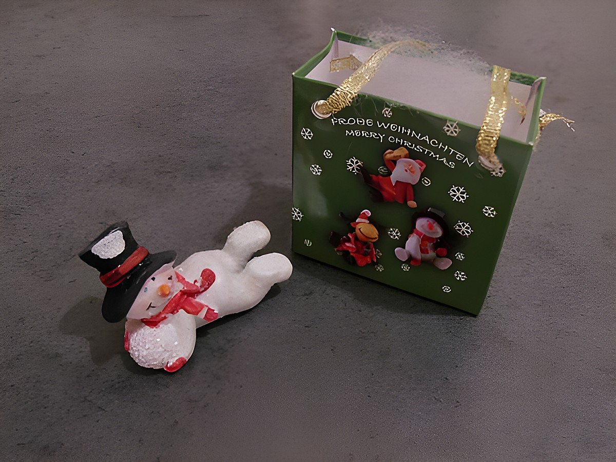 Schneemann mit Geschenktasche liegend neben einer Schneekugel, Hersteller Juwelier Harnisch, festliche Weihnachtsdekoration.