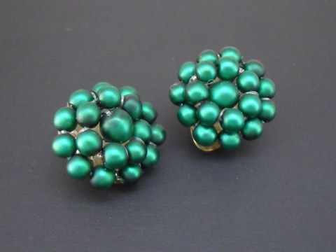 Ohrclip in dunkelgrün mit perlenteiligem Design aus goldfarbenem Material und seidenmatten synthetischen Zuchtperlen, Hersteller Juwelier Harnisch.