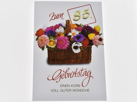 Eine Geburtstagskarte mit einem bunten Blumenkorb, ergänzt durch die Aufschrift "Zum 85. Geburtstag" und dem Text "Einen Korb voll guter Wünsche", hergestellt von Juwelier Harnisch.