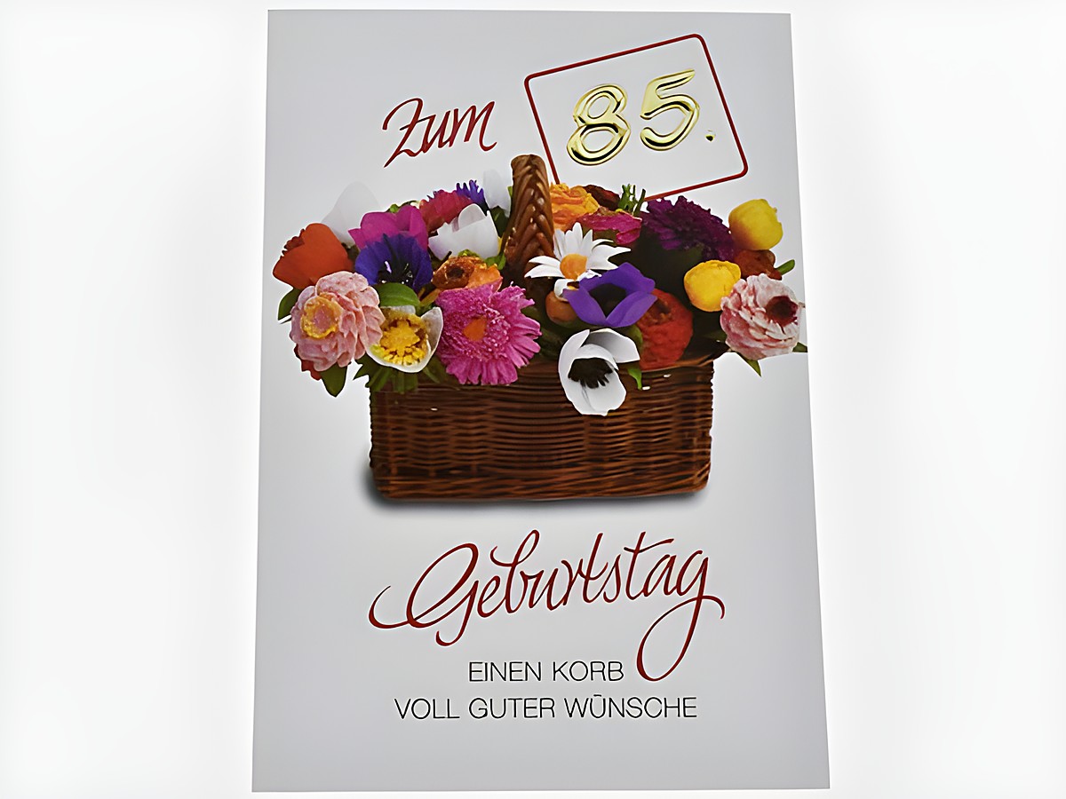 Eine Geburtstagskarte mit einem bunten Blumenkorb, ergänzt durch die Aufschrift "Zum 85. Geburtstag" und dem Text "Einen Korb voll guter Wünsche", hergestellt von Juwelier Harnisch.