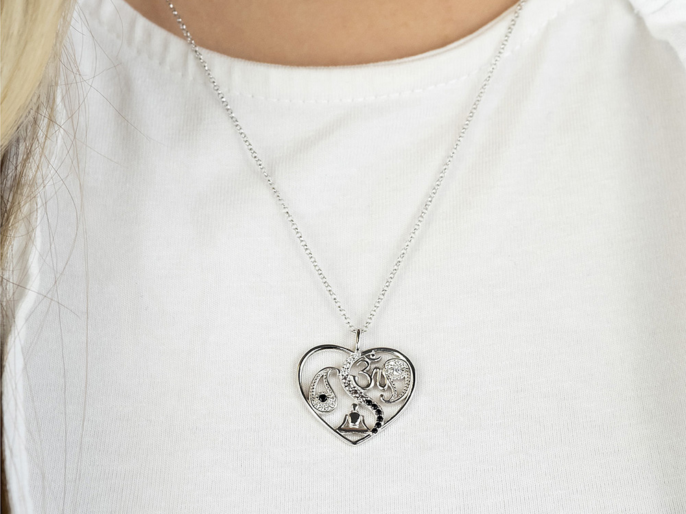 Silberne Kette mit herzförmigem Anhänger, der ein Yin Yang Symbol und Zirkonia enthält, getragen von einer Person mit heller Bluse, Länge der Kette 42 plus 4 plus 4 cm.