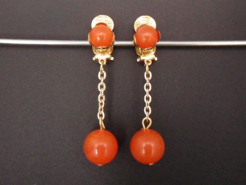 Ohrclip in orangebraun aus Kunstharz mit goldfarbenen Details, zeitloses Design von Juwelier Harnisch, elegant und ansprechend für jeden Anlass.