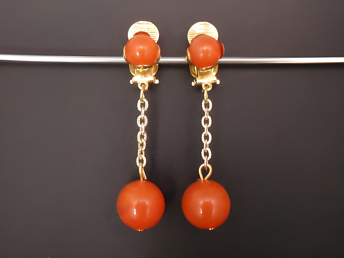 Ohrclip in orangebraun aus Kunstharz mit goldfarbenen Details, zeitloses Design von Juwelier Harnisch, elegant und ansprechend für jeden Anlass.