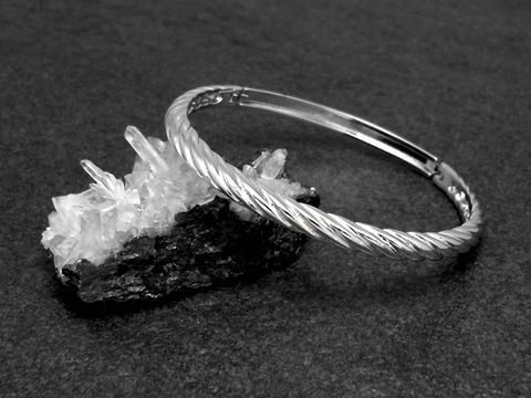 Silber Armreifen verdreht echt Silber rhodiniert mit einem Durchmesser von 16,5 cm auf einem schwarzen Untergrund neben einem Kristallstück platziert, Hersteller Juwelier Harnisch.