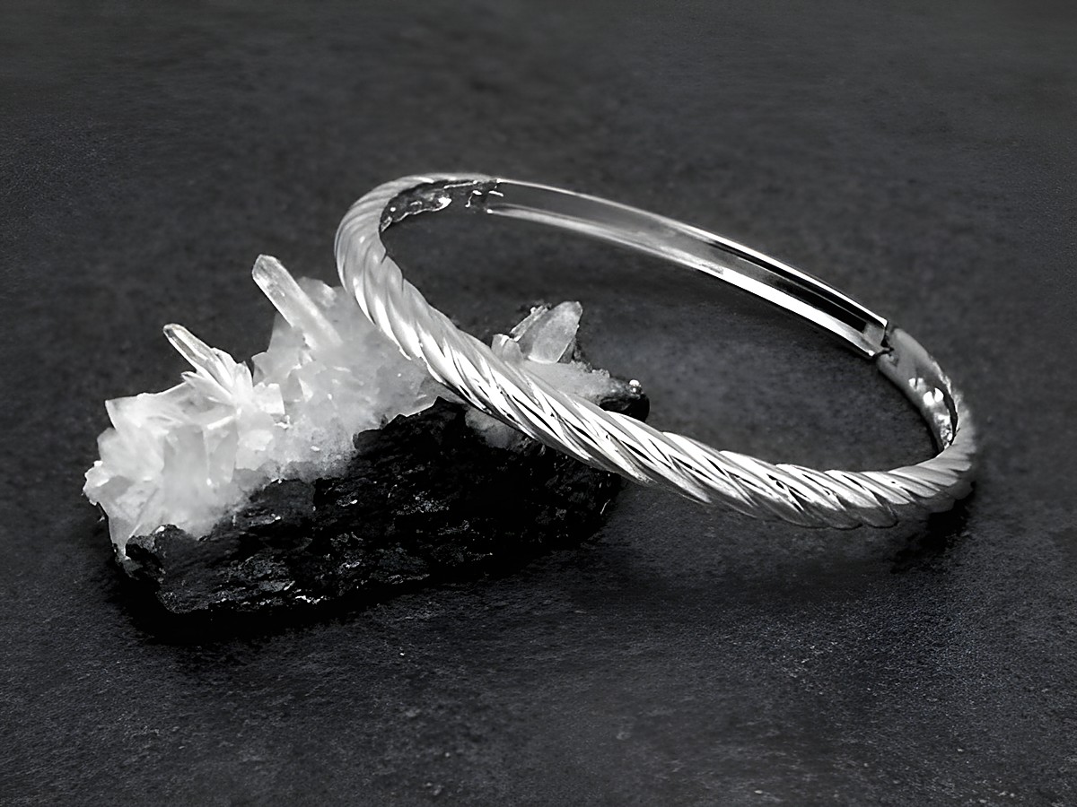 Silber Armreifen verdreht echt Silber rhodiniert mit einem Durchmesser von 16,5 cm auf einem schwarzen Untergrund neben einem Kristallstück platziert, Hersteller Juwelier Harnisch.