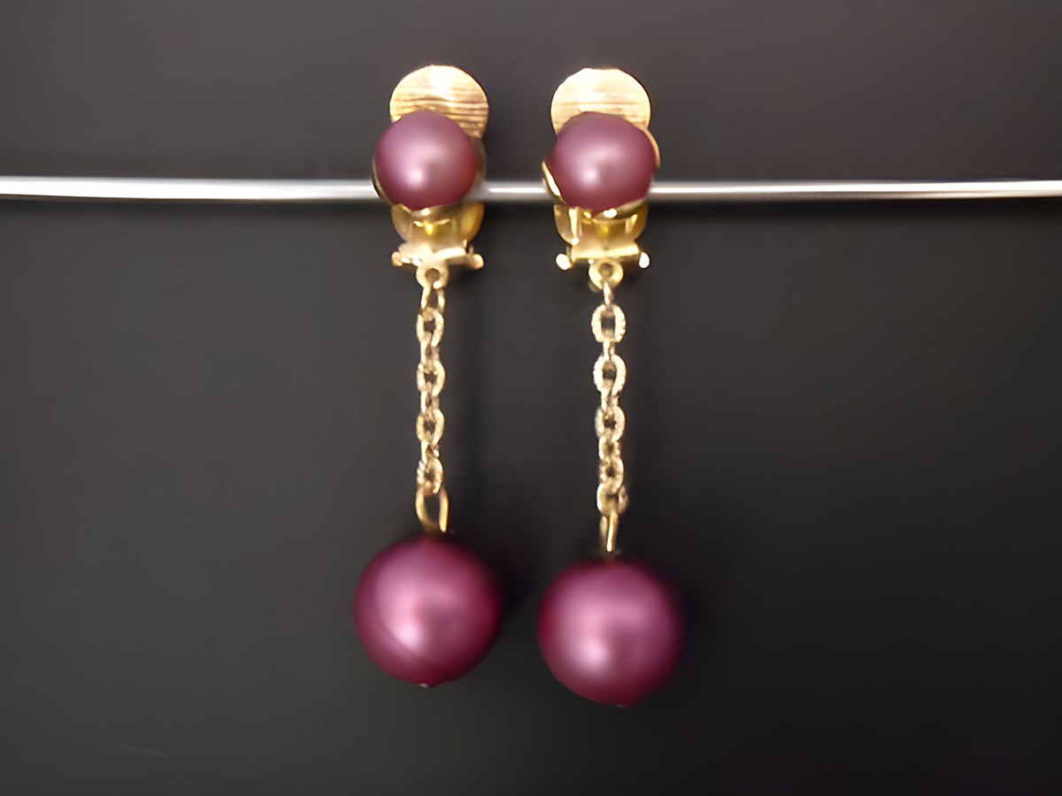 Ohrclip in rotlila matt mit goldfarbenen Details. Hergestellt aus Kunstharz, zeitloses Design von Juwelier Harnisch. Schmuckstück mit eleganter Ausstrahlung.