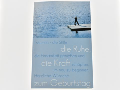 Eine Geburtstagskarte mit dem Motiv eines Stegs am Wasser, auf dem eine Person steht. Der Text auf der Karte spricht von Träumen, Ruhe und Kraft sowie herzlichen Geburtstagswünschen. Hersteller: Juwelier Harnisch.