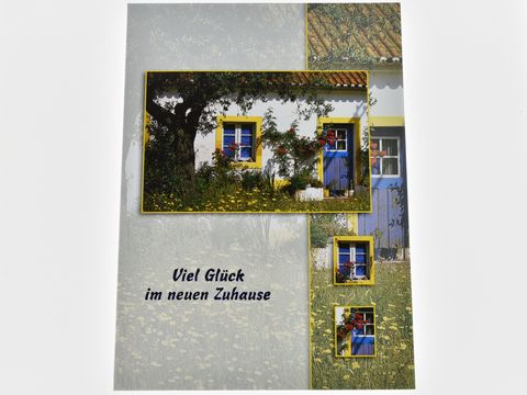Eine Grußkarte zeigt ein Haus mit blauer Tür und Fensterladen, umgeben von Rosen und einem Baum. Die Karte wünscht viel Glück im neuen Zuhause und stammt vom Juwelier Harnisch.
