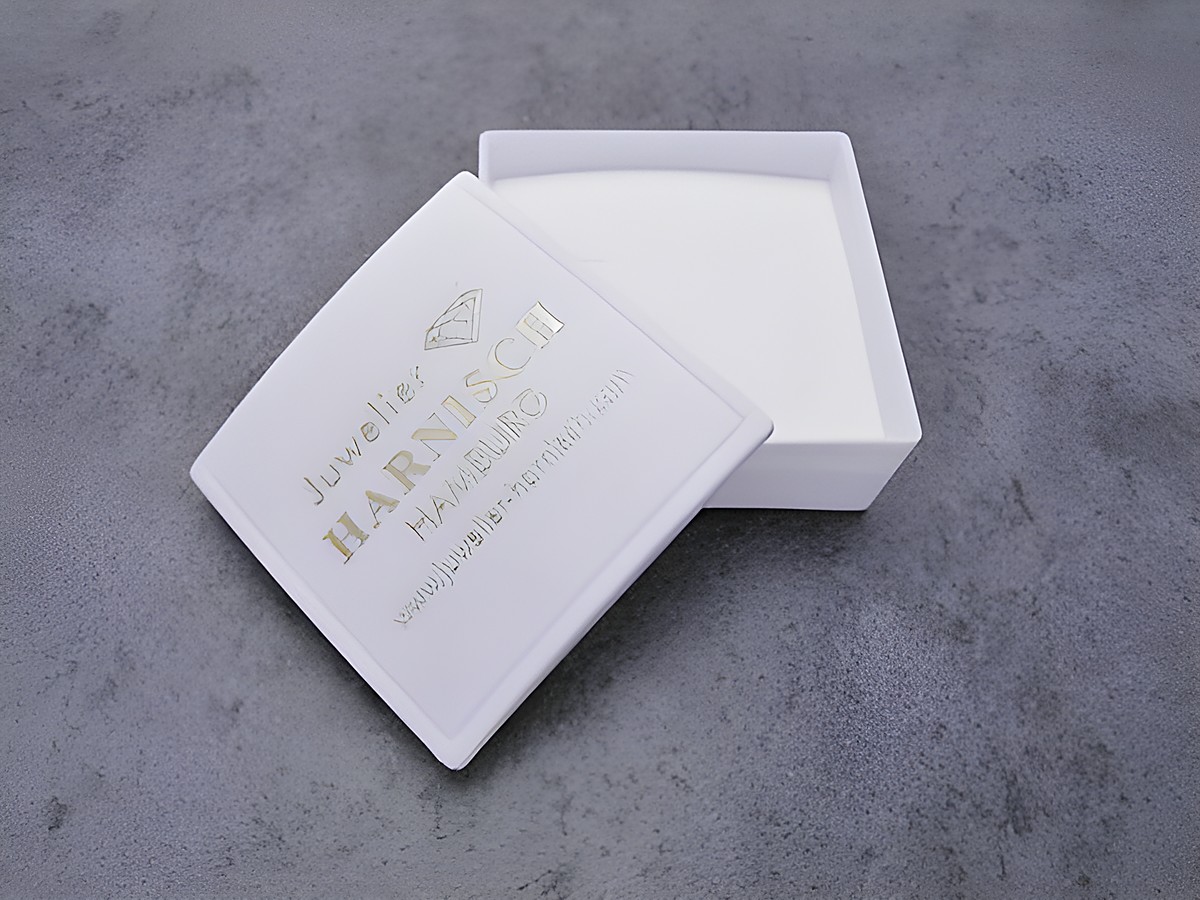 Geschenkschachtel 4 x 4 cm von Juwelier Harnisch, weiß mit goldener Prägung, geöffnet, innen mit weichem Material ausgekleidet, ideal für Schmuckgeschenke. – Ansicht 2