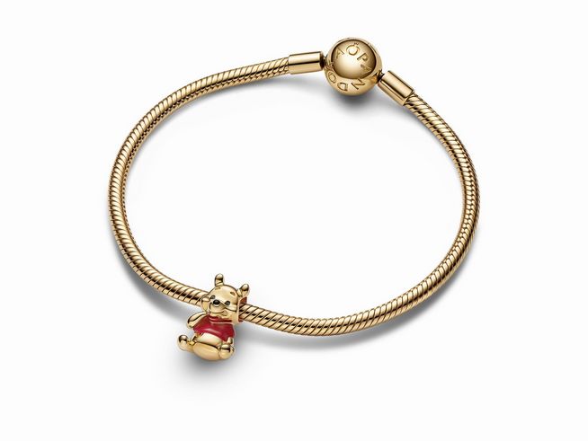 Charm mit Winnie Puuh Bär aus gelbgoldvergoldetem Material, der auf einem feinen Armband sitzt. Ein farbenfrohes Design zum Sammeln und Verschenken, hergestellt von Pandora Disney.
