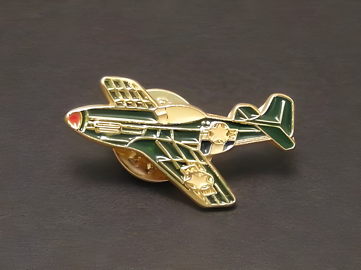 Segelflugzeug grün Pin Anstecker Anstecknadel des Herstellers Juwelier Harnisch, Darstellung eines stilisierten Flugzeugs mit goldenen Details und roter Nasenspitze auf dunklem Hintergrund.
