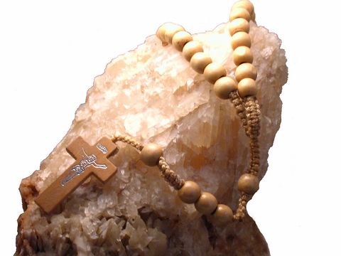 Rosenkranz aus echtem Holz in hellbraun, 47 cm lang, von Juwelier Harnisch, mit einem Kreuz und Edelsteinen, auf einem hellen Kristallhintergrund platziert.