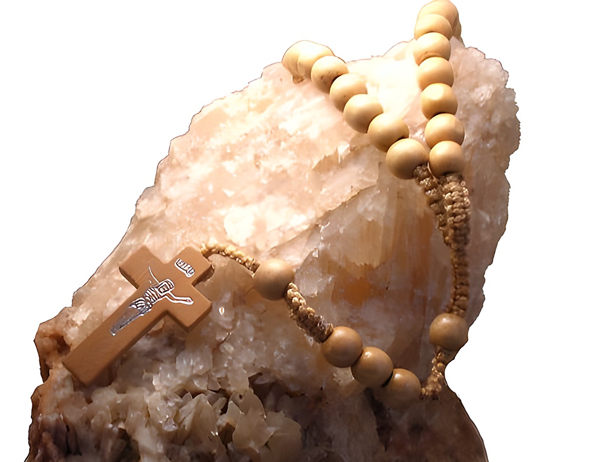 Rosenkranz aus echtem Holz in hellbraun, 47 cm lang, von Juwelier Harnisch, mit einem Kreuz und Edelsteinen, auf einem hellen Kristallhintergrund platziert.