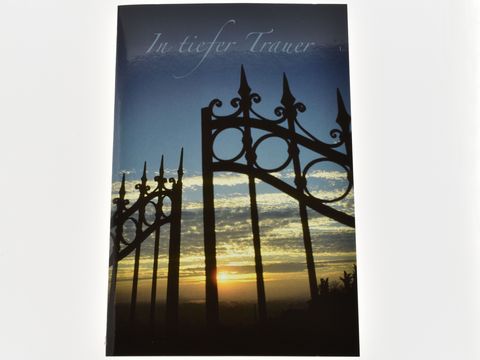 Ein Abendhimmel mit einem Tor im Vordergrund, die Farben des Sonnenuntergangs reflektieren Traurigkeit. Der Schriftzug In tiefer Trauer ist dezent platziert. Trauerkarte von Juwelier Harnisch.