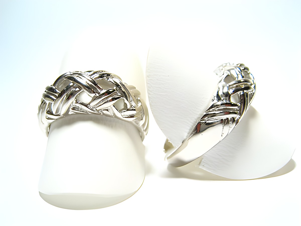 Silber Ring rhodiniert aus den 70er Jahren, verstellbar, Hersteller: Juwelier Harnisch, ohne Stein, mit ansprechendem Geflechtsdesign, auf weißen Ringpräsentern abgebildet.