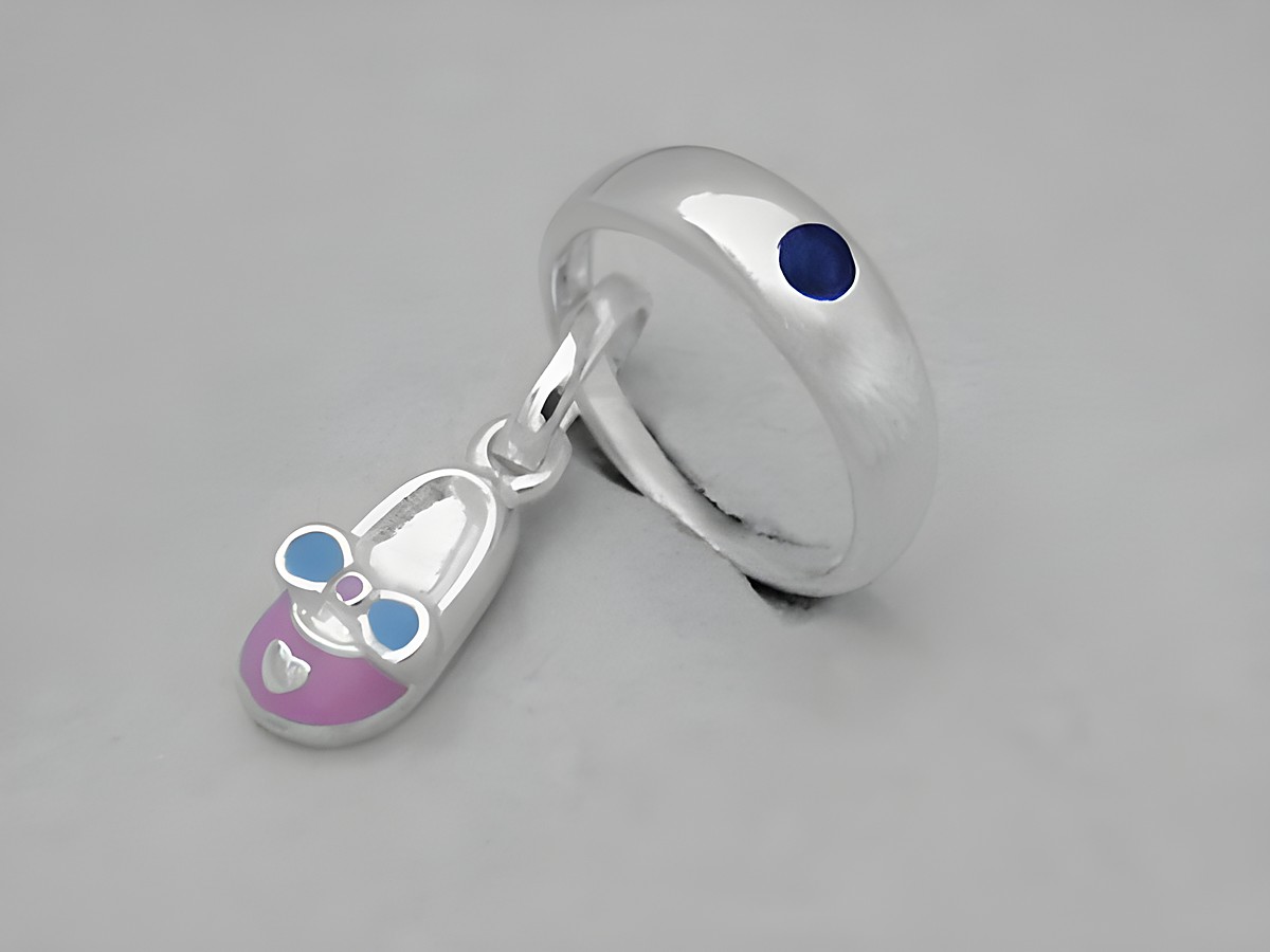 Silber Taufring mit rosa Schuh SAFIR, Hersteller Juwelier Harnisch, zeigt einen filigranen Anhänger in Form eines Babyschuhs mit blauem und rosa Design.