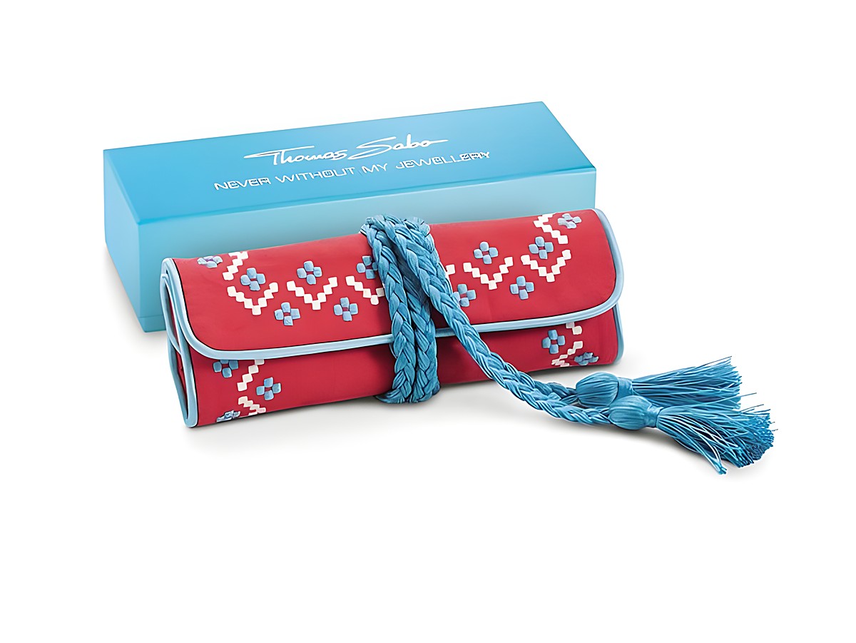 Schmuckrolle von Thomas Sabo in rot und türkis mit ethnischem Muster, geflochtenem Verschluss und Quasten, präsentiert in einer blauen Geschenkbox. Ideal zur Aufbewahrung von Schmuck.