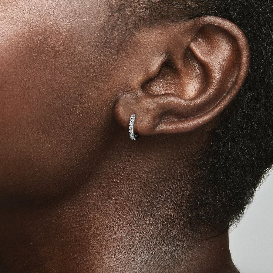 Funkelnde Huggie Ohrringe von Pandora aus Sterling Silber mit Zirkonia, 1 cm, sind im Ohr einer Person zu sehen, die ein neutrales Gesicht zeigt und einen dezenten Look präsentiert.
