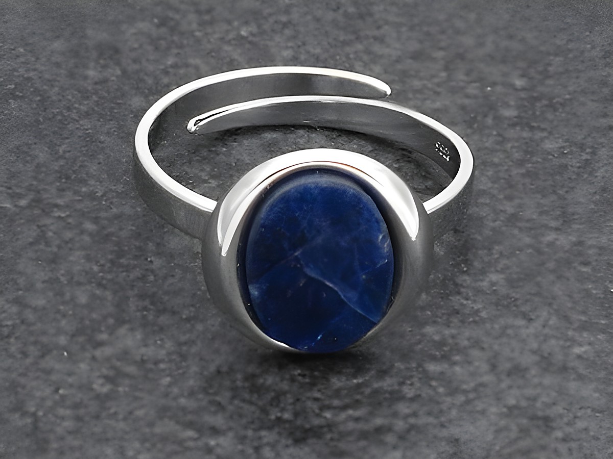 Silberring in ovaler Form, verstellbar, mit einem Sodalithstein, rhodiniert, Hersteller Juwelier Harnisch. Der Ring präsentiert sich elegant und modern auf einem dunklen Hintergrund.