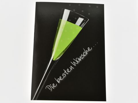 Geburtstagskarte mit einem Sektglas, das mit grünem Inhalt gefüllt ist. Im Hintergrund schwarze Farbe und der Schriftzug Die besten Wünsche. Hersteller ist Juwelier Harnisch.