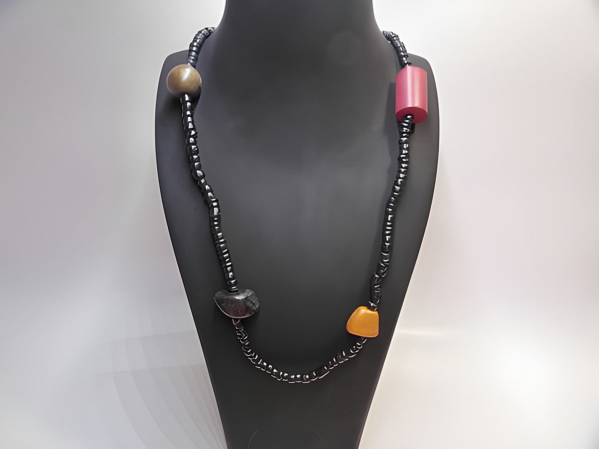 Holzkette Multiform 23 mm bunt 90 cm Holz Schmuck von Juwelier Harnisch, präsentiert auf einem schwarzen Hals display, zeigt farbige Holzperlen und unterschiedliche Formen.