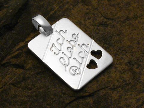Ein Anhänger aus Sterling Silber mit der gravierten Aufschrift Ich liebe Dich und zwei Herzen, hergestellt von Juwelier Harnisch, ideal als Geschenk oder Liebesbotschaft.