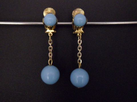 Ohrclip in himmelblau mit zeitlosem Design, goldfarbene Elemente und Kunstharz, hergestellt von Juwelier Harnisch, eleganter Schmuck mit einer Kette und einer runden Perle.