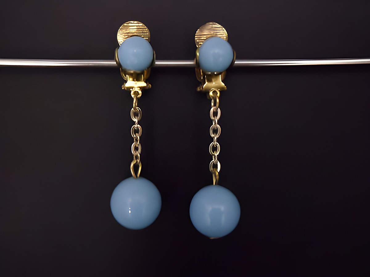 Ohrclip in himmelblau mit zeitlosem Design, goldfarbene Elemente und Kunstharz, hergestellt von Juwelier Harnisch, eleganter Schmuck mit einer Kette und einer runden Perle.