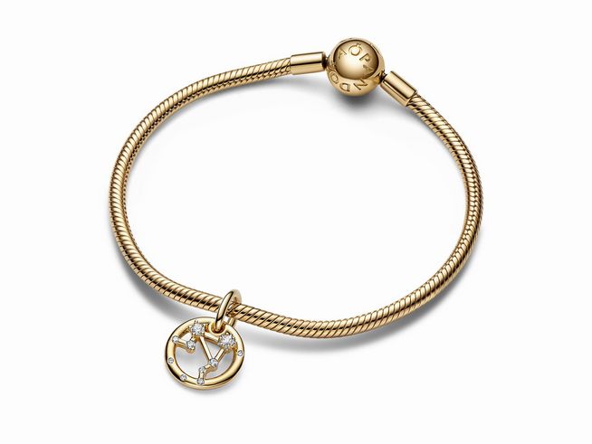 Der elegante Charm-Anhänger zeigt das Sternzeichen Waage in gelbgold vergoldeter Ausführung, verziert mit funkelndem Zirkonia, angebracht an einem hochwertigen Armband von Pandora.