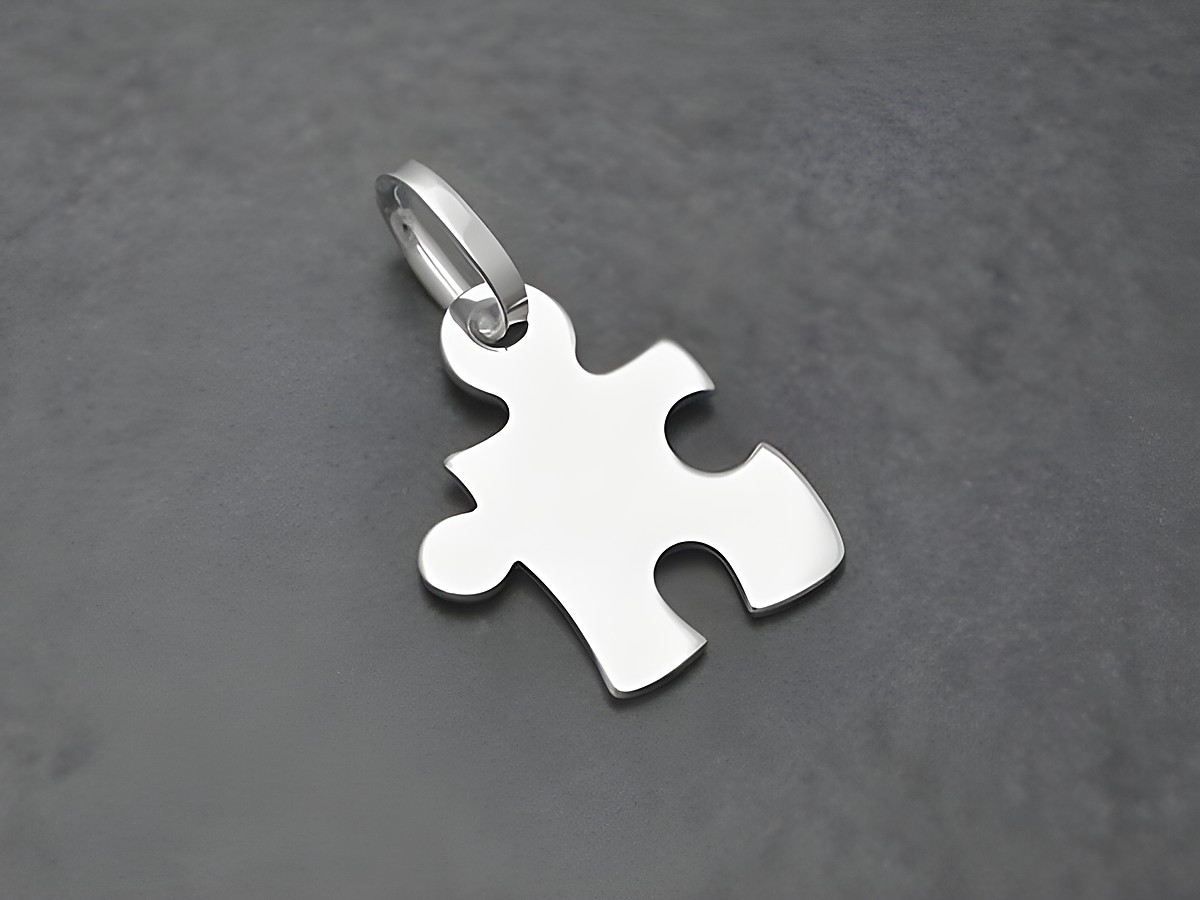 Puzzle Teil aus Sterling Silber Anhänger von Juwelier Harnisch, Partner, auf grauem Hintergrund. Der Anhänger zeigt eine glatte, stilisierte Puzzlestück-Form.