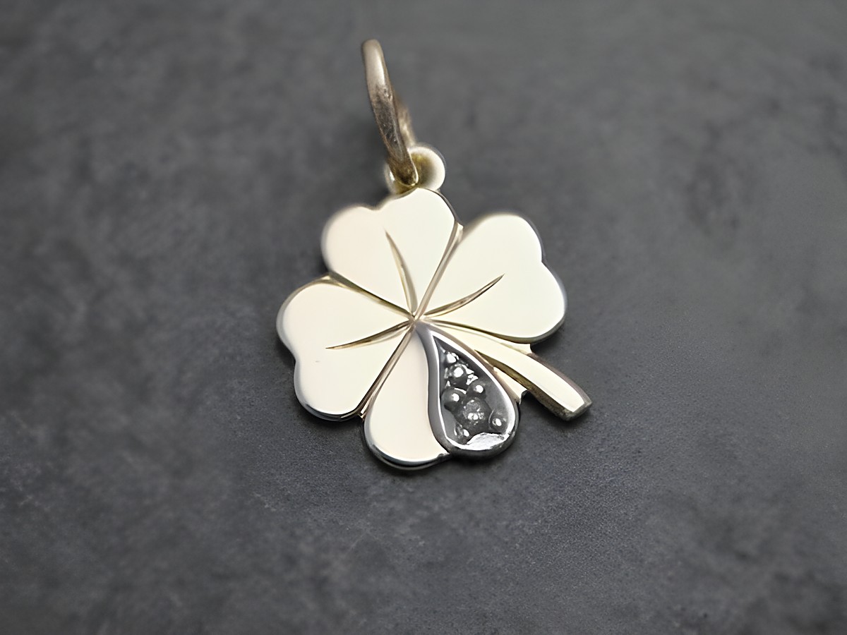 Ein goldener Anhänger in Form eines Kleeblatts mit einem diamantenen Glücksbringer, hergestellt von Juwelier Harnisch, symbolisiert Glück und Wohlstand.