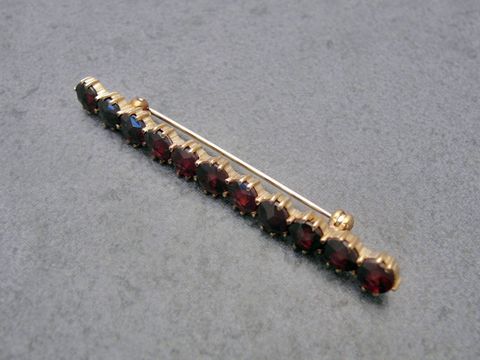 Dezente Gold Brosche mit Granatschmuck, 56,9 mm lang, gefertigt vom Juwelier Harnisch, mit mehreren rot schimmernden Granatsteinen. Ideal als elegantem Accessoire.