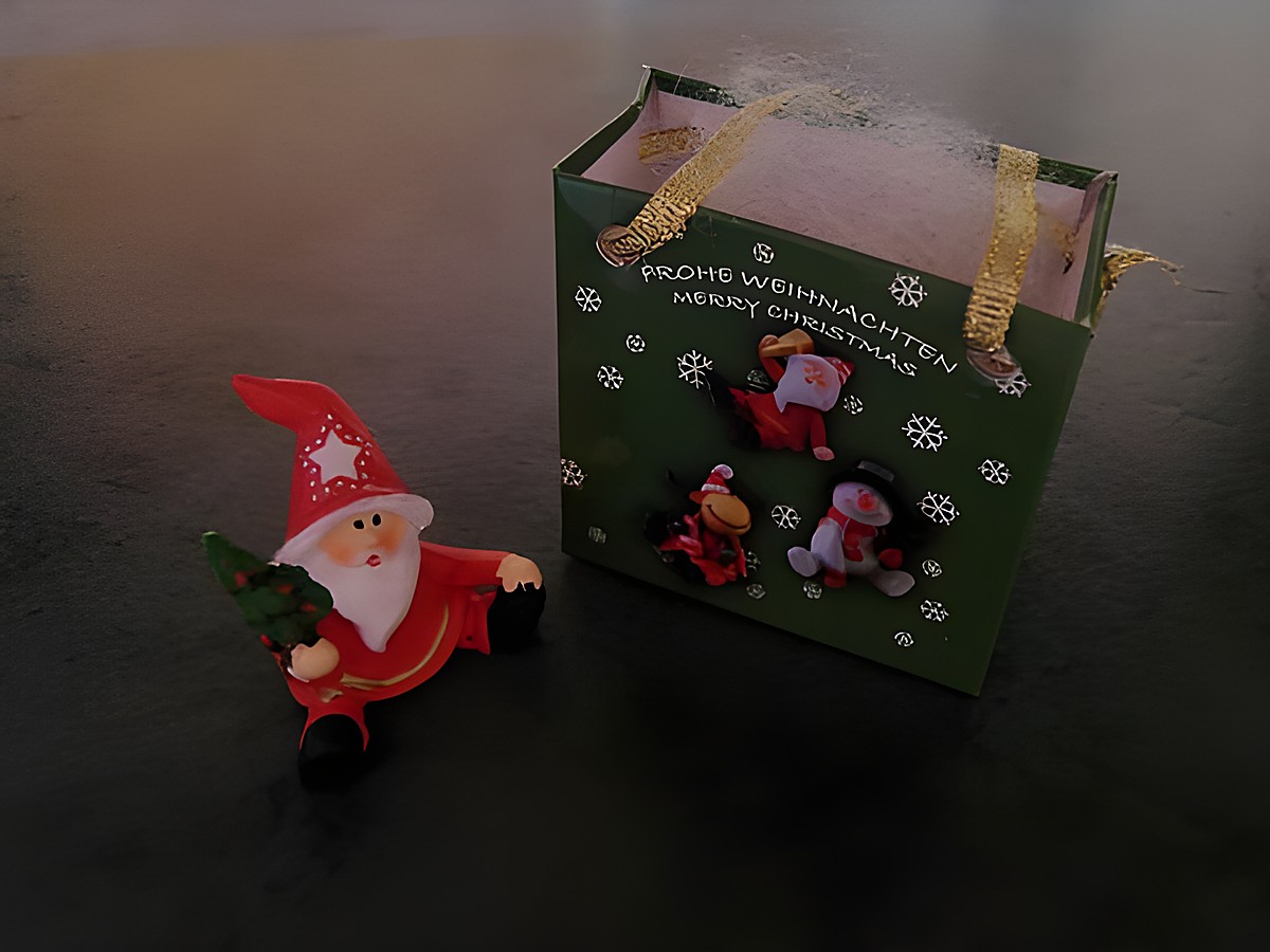 Weihnachtsmann mit Geschenktasche sitzt neben einem Tannenbaum, umgeben von einer grünen Geschenkebox mit Weihnachtsmotiven, Hersteller: Juwelier Harnisch, Weihnachten.