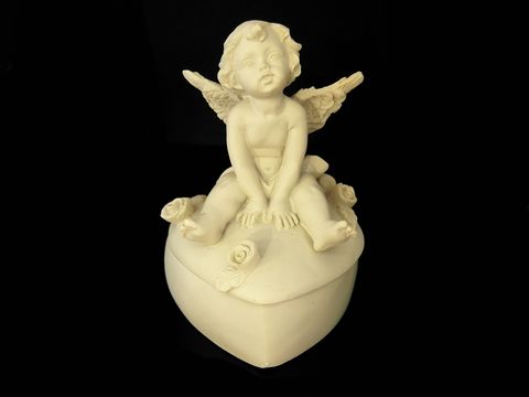 Eine sitzende Schutzengel Figur auf einer herzförmigen Dose, gefertigt von Juwelier Harnisch, ideal als Geschenkidee, verziert mit kleinen Rosenblüten.