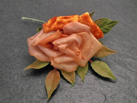 Verspielter Haarschmuck in Form einer orangefarbenen Blume aus Samt-Mix mit grünen Blättern, ideal für besondere Anlässe, Hersteller Juwelier Harnisch.