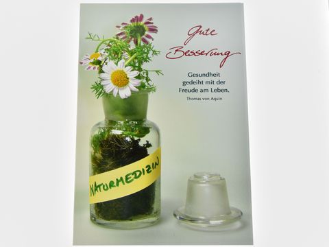 Auf dem Bild ist eine Genesungskarte zu sehen, auf der eine Flasche mit verschiedenen Pflanzen und einem gelben Label mit dem Wort Naturmedizin abgebildet ist, der Text Gute Besserung ergänzt das Motiv.
