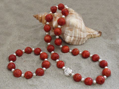 Korallenschmuck Set bestehend aus einer Kette und einem Armband mit Zuchtperlen in rot, hergestellt von Juwelier Harnisch, Korallenketten in ansprechender Präsentation neben einer Muschel.