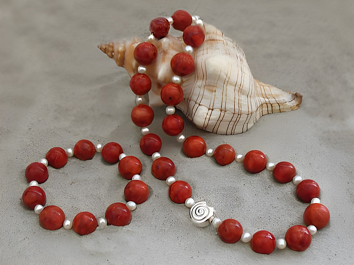 Korallenschmuck Set bestehend aus einer Kette und einem Armband mit Zuchtperlen in rot, hergestellt von Juwelier Harnisch, Korallenketten in ansprechender Präsentation neben einer Muschel.
