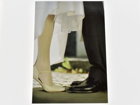Eine Hochzeitskarte mit einer Nahaufnahme der Füße eines Brautpaares. Die Braut trägt einen weißen Schleier und elegante Schuhe, der Bräutigam trägt schwarze Schuhe und einen Anzug.