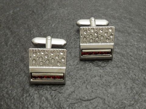 Silberfarbene Manschettenknöpfe vom Juwelier Harnisch mit roten Strass Steinen, elegantes Design mit strukturierter Oberfläche und funkelnden Akzenten, ideal für festliche Anlässe.