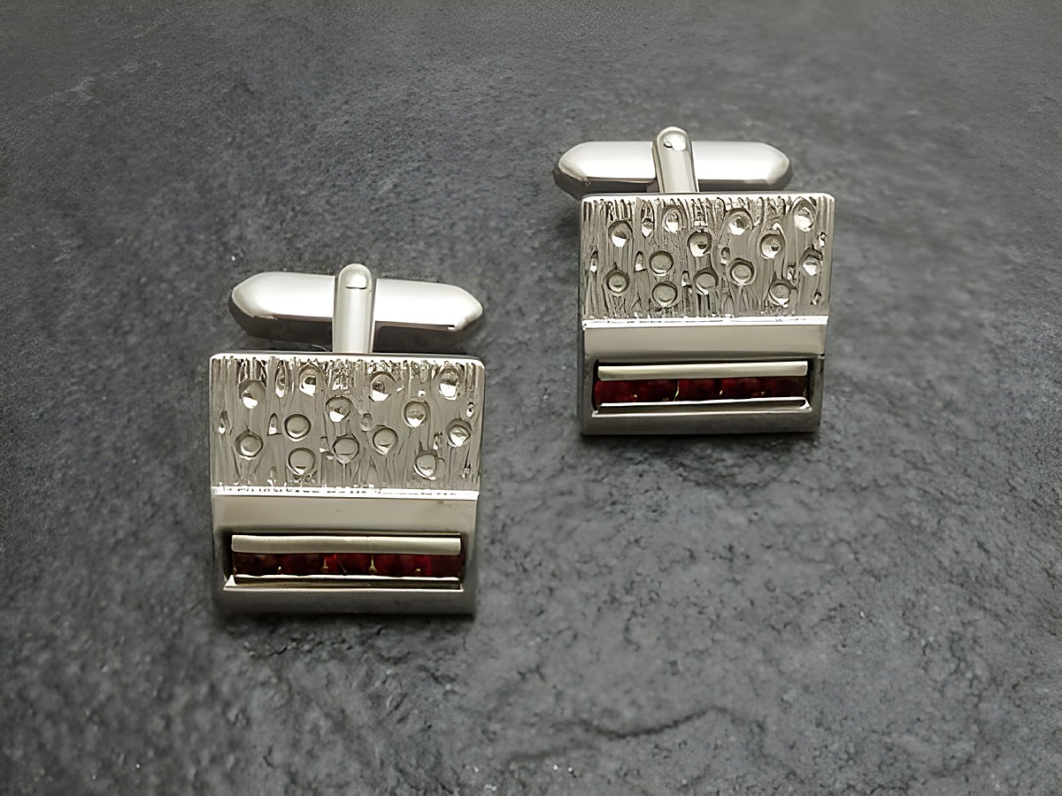 Silberfarbene Manschettenknöpfe vom Juwelier Harnisch mit roten Strass Steinen, elegantes Design mit strukturierter Oberfläche und funkelnden Akzenten, ideal für festliche Anlässe.