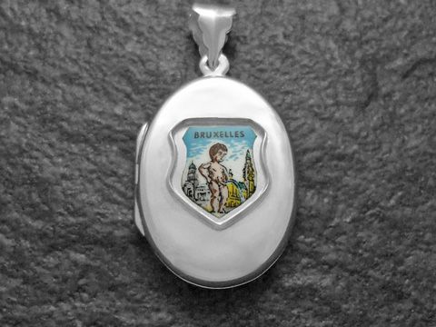 600019601-0 Ein silbernes Medaillon mit einem bunten Bild von Manneken Pinkel und der Aufschrift Bruxelles. Es ist ein elegantes Schmuckstück des Herstellers Juwelier Harnisch aus Europa.