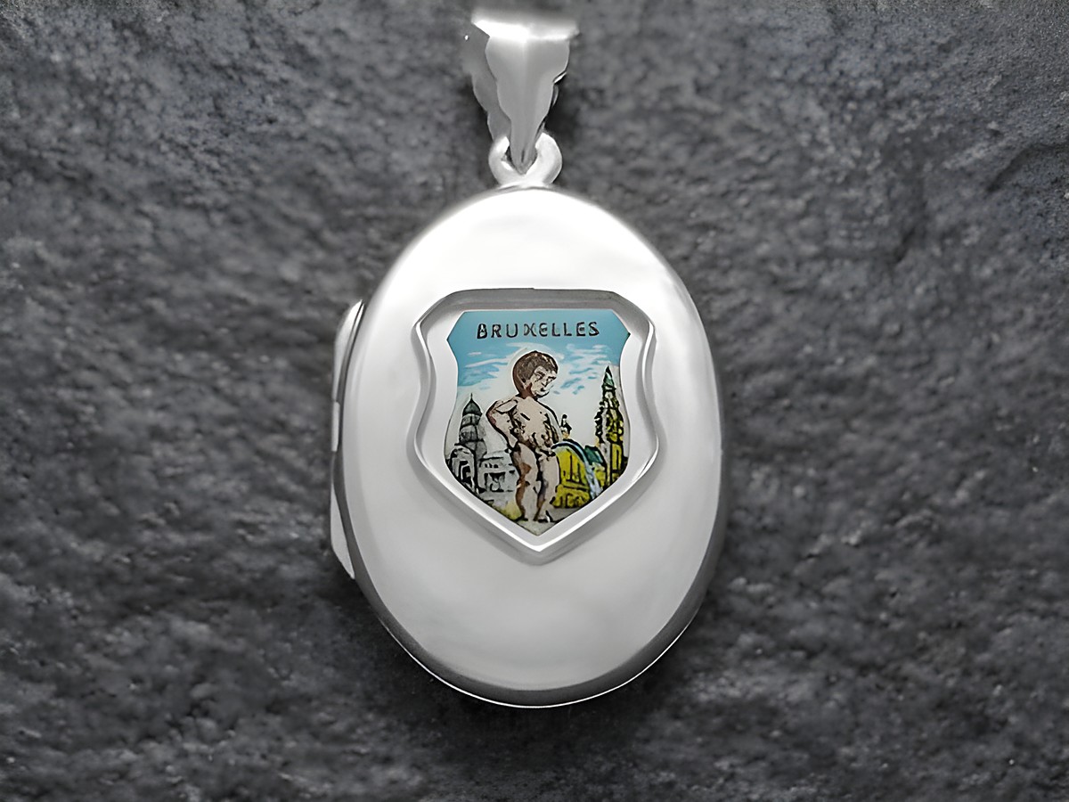 Ein silbernes Medaillon mit einem bunten Bild von Manneken Pinkel und der Aufschrift Bruxelles. Es ist ein elegantes Schmuckstück des Herstellers Juwelier Harnisch aus Europa.