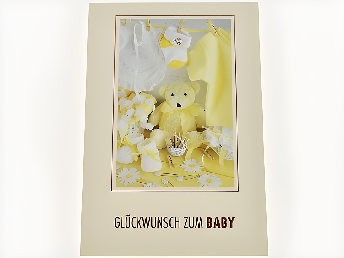 Glückwunschkarte zur Geburt eines Babys mit verschiedenen Baby-Sachen in Gelb und Weiß, darunter ein Teddybär, Babykleidung und Accessoires, Hersteller Juwelier Harnisch.